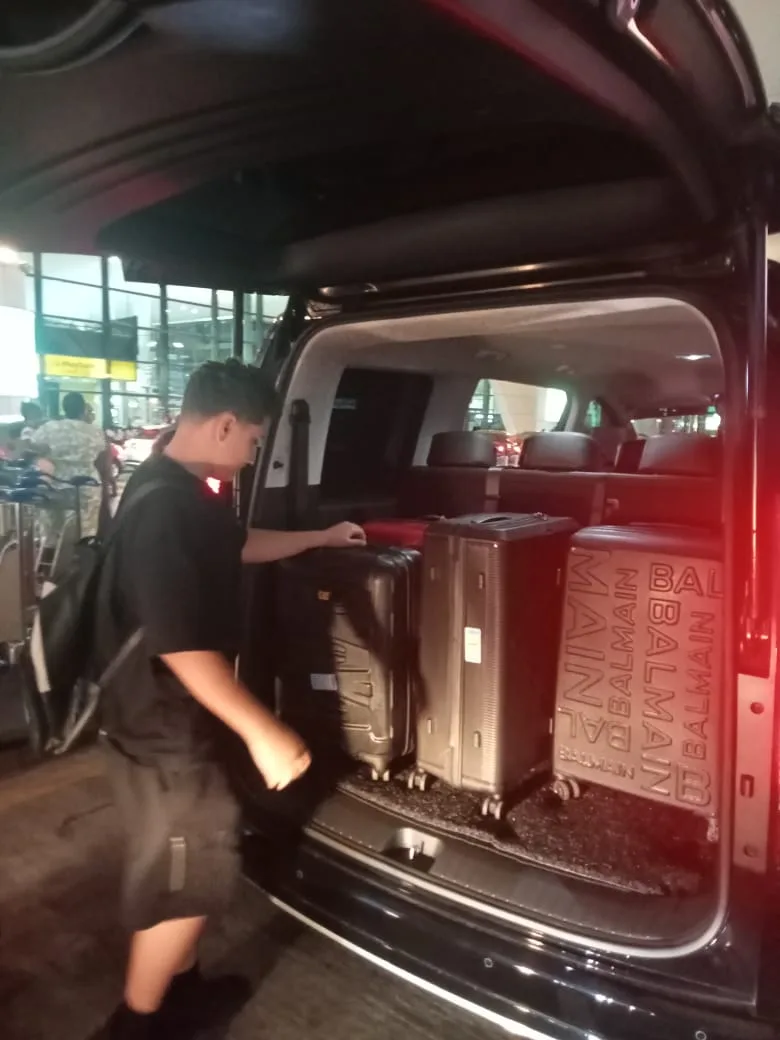 Driver loading designer luggage into Alphard boot at airport at night