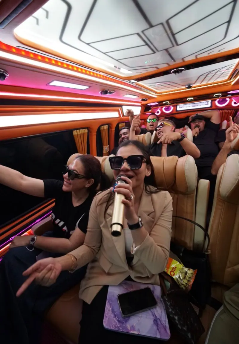 Group singing karaoke inside luxury van with ambient lighting during trip