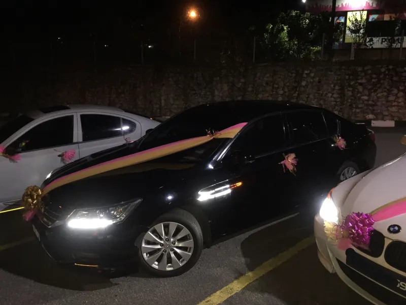 Black sedan and white BMW decorated with pink and gold wedding ribbons at night